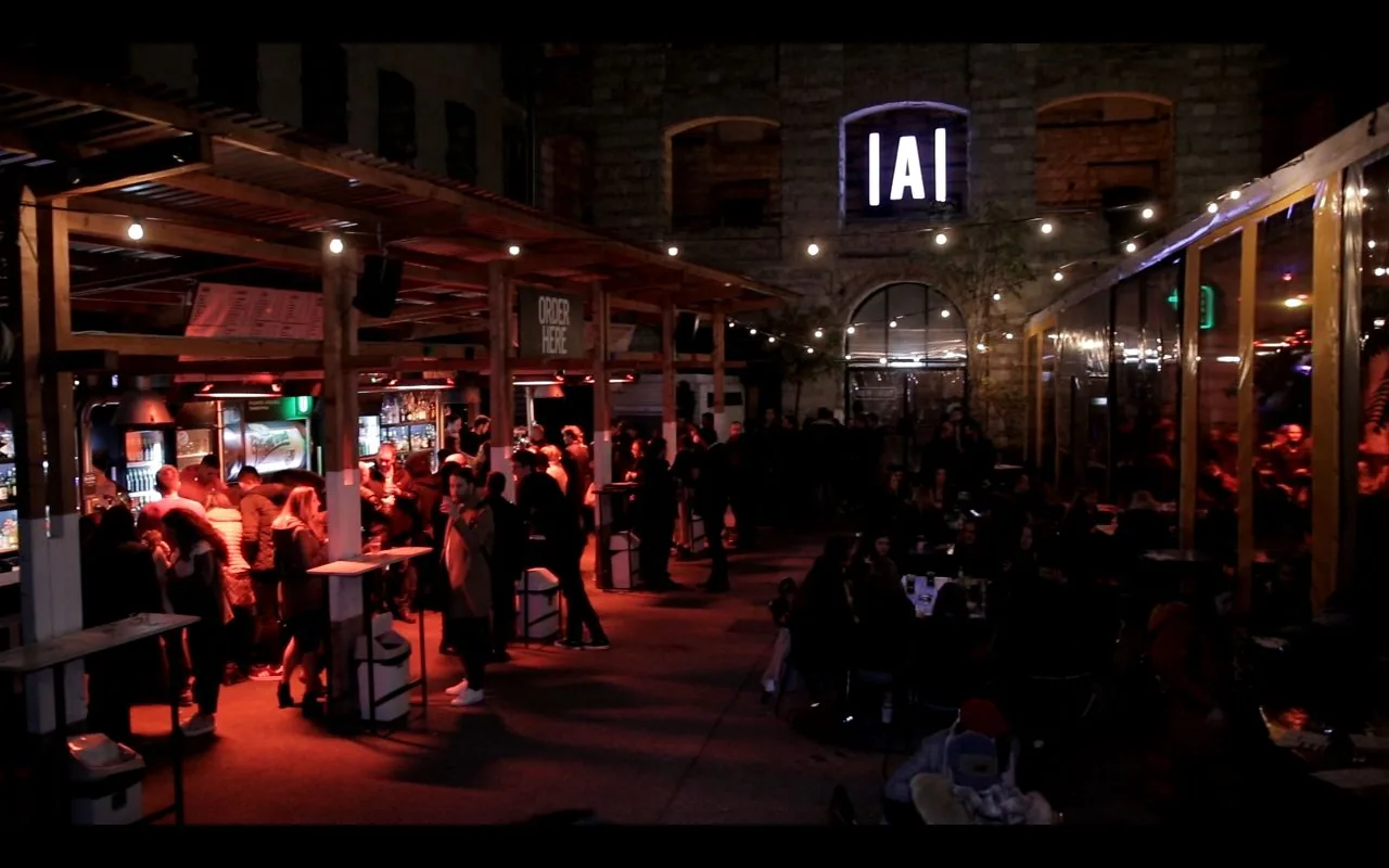 Anker't's industrial open-air courtyard with a wooden pergola and string lights beneath its lit 'A' sign, Budapest