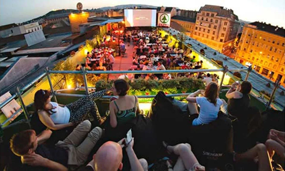 Corvintető's rooftop terrace at dusk — an open-air bar with an outdoor cinema screen and panoramic city skyline views over central Budapest