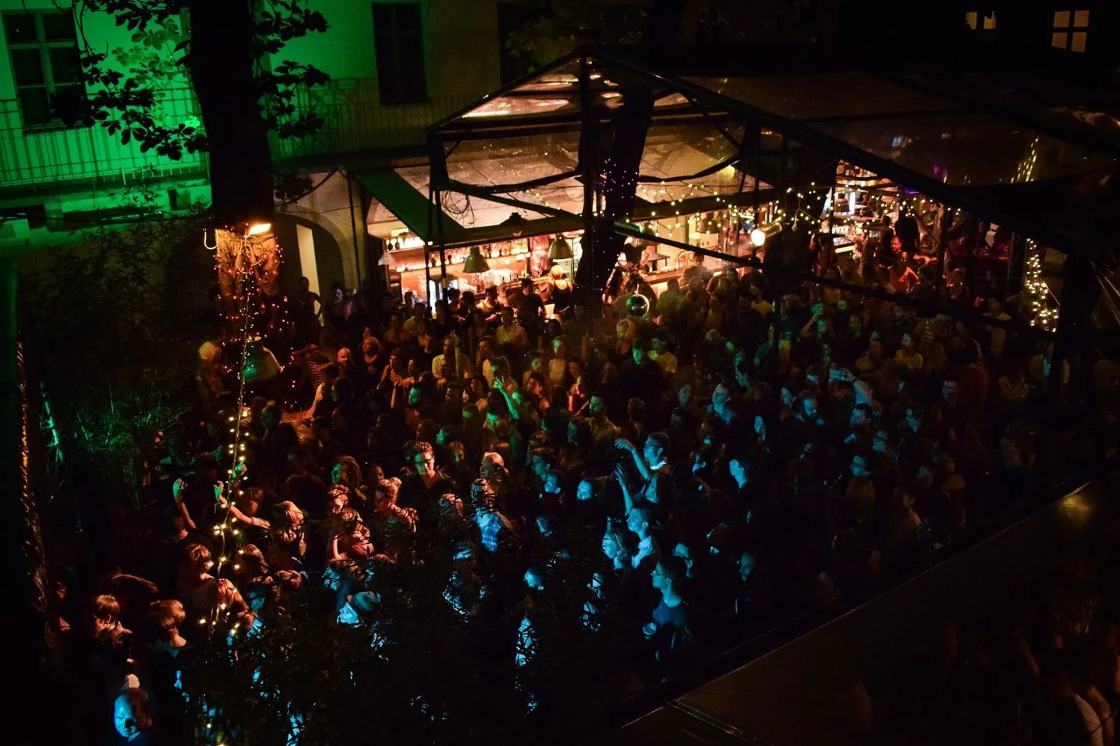 A night-time crowd dancing under a marquee in the busy courtyard of Ellátóház, Budapest