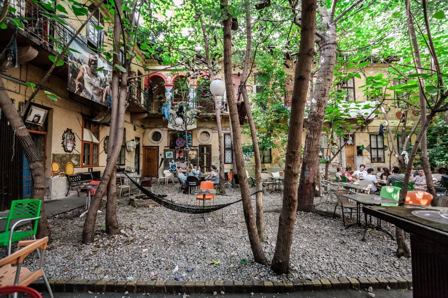 Grandió's tree-filled gravel courtyard with a hammock and street-art-covered walls — the 'jungle' ruin-bar garden, Budapest